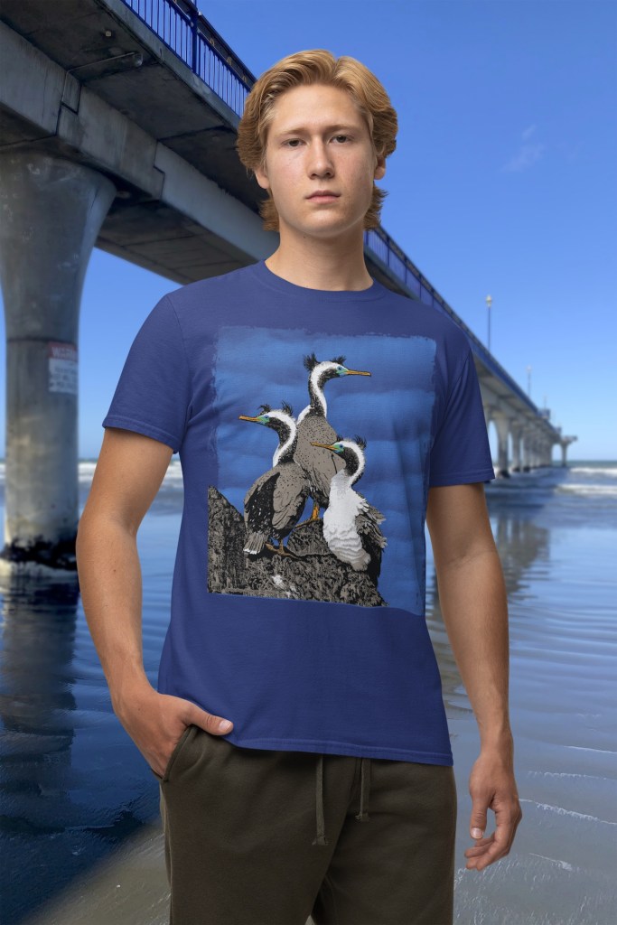 Front view of a young man wearing a Surface Active spotted shags t-shirt beside New Brighton pier.