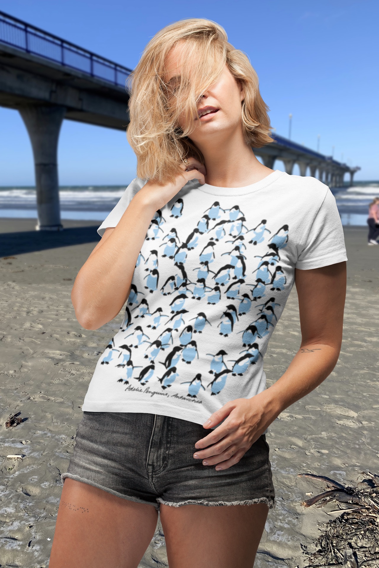 Young woman modeling an all-over printed Adelie Penguin t-shirt by the reinforced concrete New Brighton Pier in Christchurch, New Zealand.