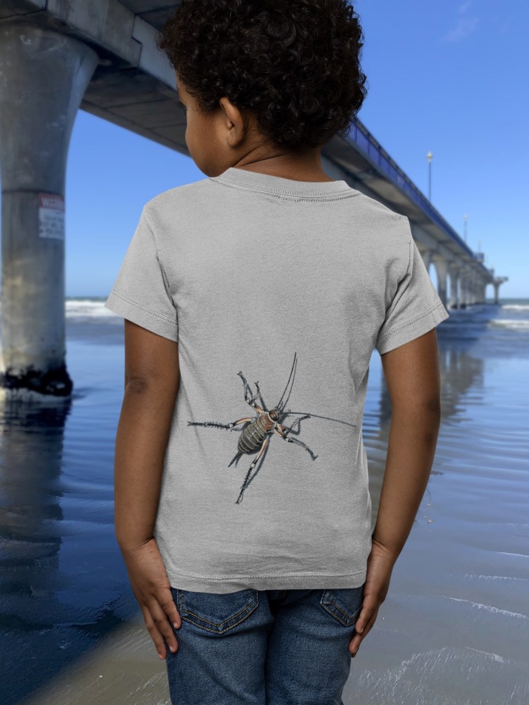 Back view of a child in a grey marle t-shirt with an all-over weta print, standing near New Brighton Pier, facing the sea.