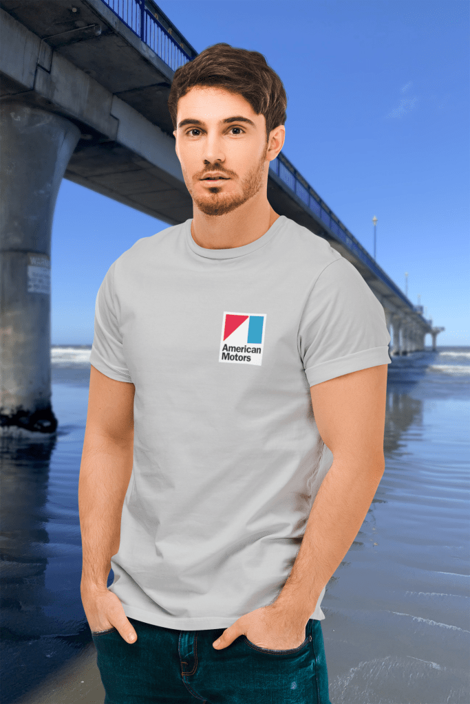A man in a grey marle t-shirt featuring an American Motors logo badge, standing beside New Brighton Pier, which visually extends like a concrete path towards the horizon.
