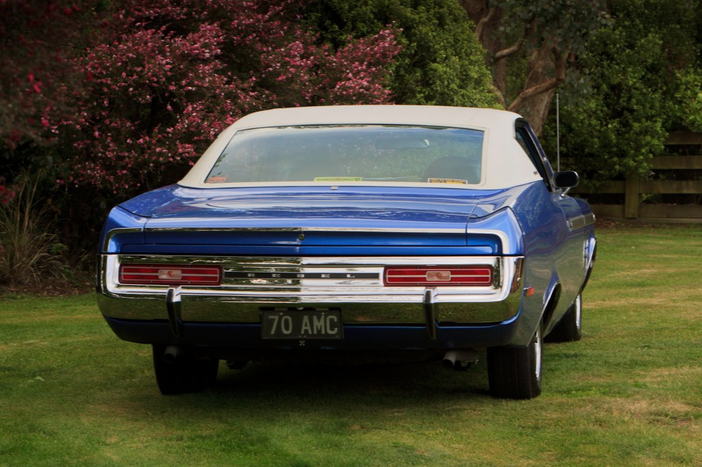 Royal blue 1970 Rambler Rebel SST seen from a rear oblique angle, highlighting tail lights, trunk, and bumper, showcasing the car's restored elegance.