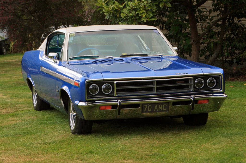Front and side view of a restored 1970 Rambler Rebel SST in royal blue, showcasing the hood, grille, and bumper from a mid-windshield perspective.