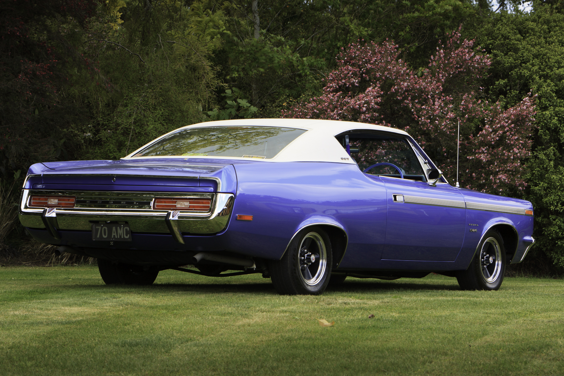 Low angle three-quarter rear view of a restored royal blue 1970 Rambler Rebel SST, highlighting the rear bumper and distinctive tail lights.