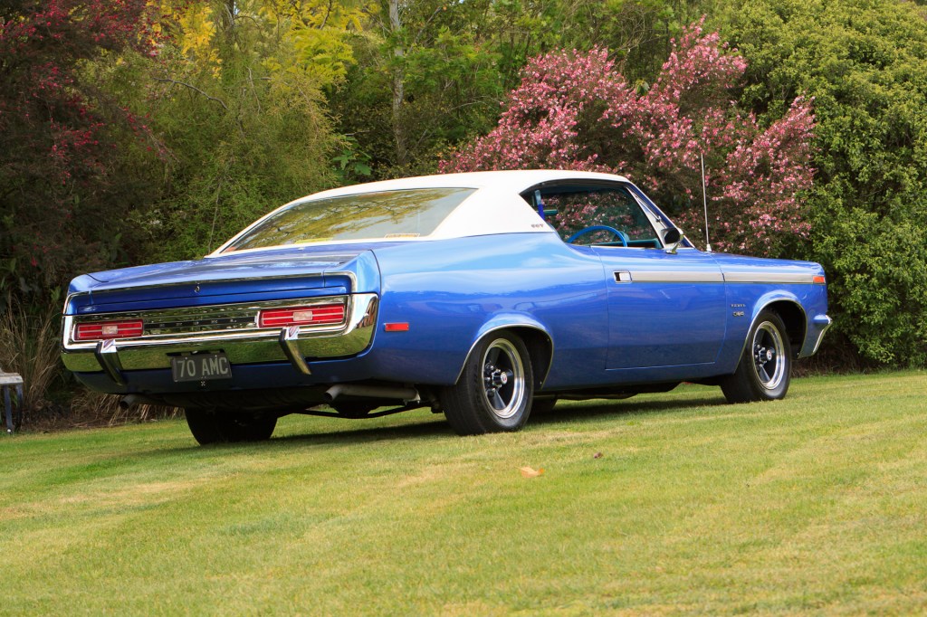 Low-angle view of a restored 1970 Rambler Rebel SST in royal blue, showcasing the rear bumper and tail lights, reflecting the car's classic muscle car design.
