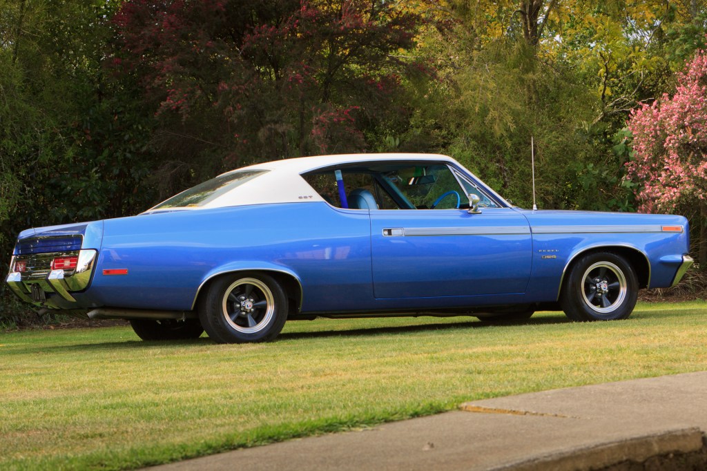 Low-angle side view of a royal blue 1970 Rambler Rebel SST showcasing the rear bumper and tail lights, highlighting the car's restored elegance.