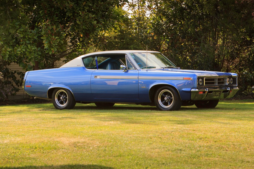 Low-angle side view of a restored 1970 Rambler Rebel SST in royal blue, showcasing the chrome bumper, grille, and classic lines of this American muscle car.