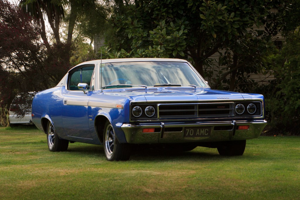 Low-angle view of a restored royal blue 1970 Rambler Rebel SST, highlighting its front grille and headlights, symbolising classic muscle car elegance.
