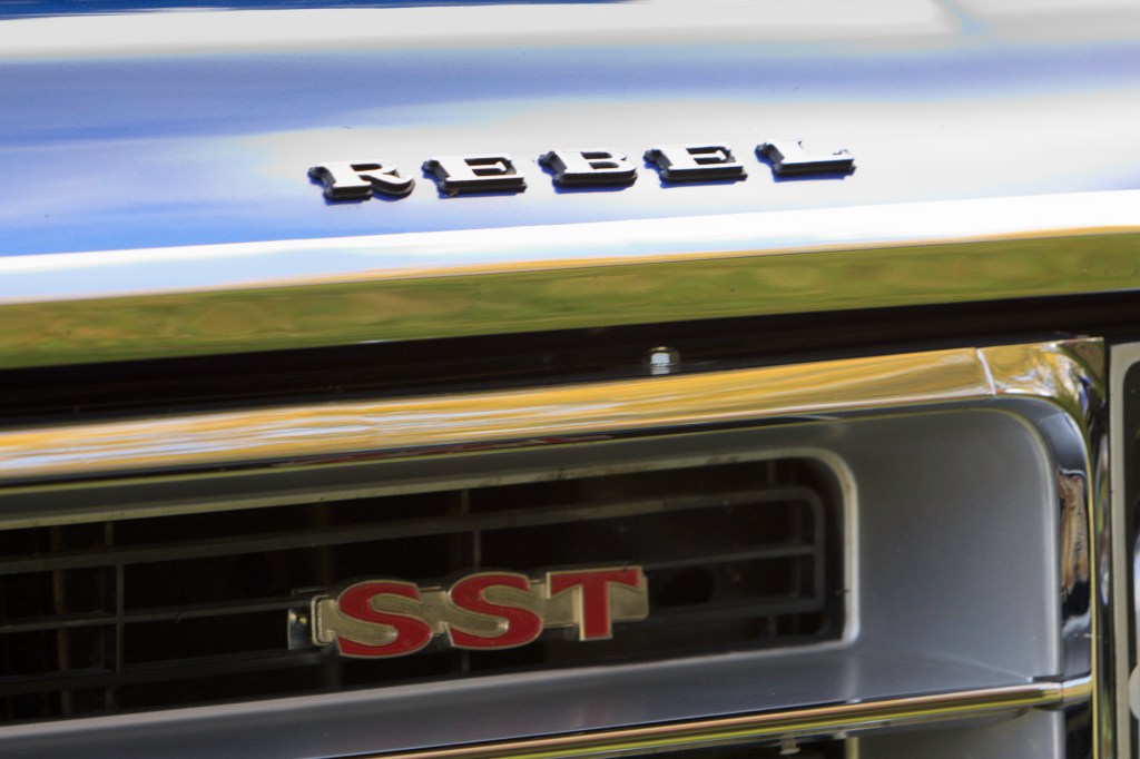 Close-up of the 'Rebel - SST' badge on the grille of a royal blue 1970 Rambler Rebel SST, showcasing the emblem's chrome finish.