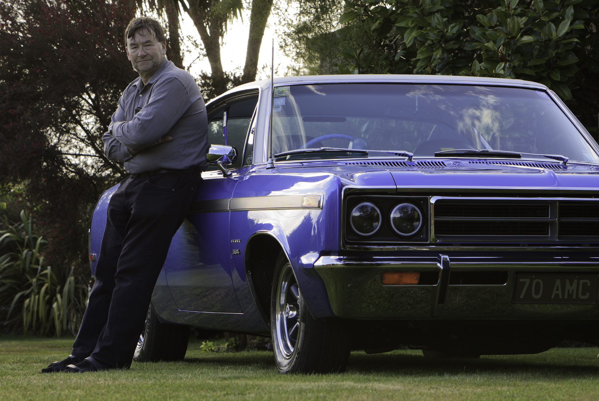 Lindsay McKenzie, with his restored 1970 Rambler Rebel SST in royal blue, leaning against the driver's door, showcasing the culmination of a 33-year quest.
