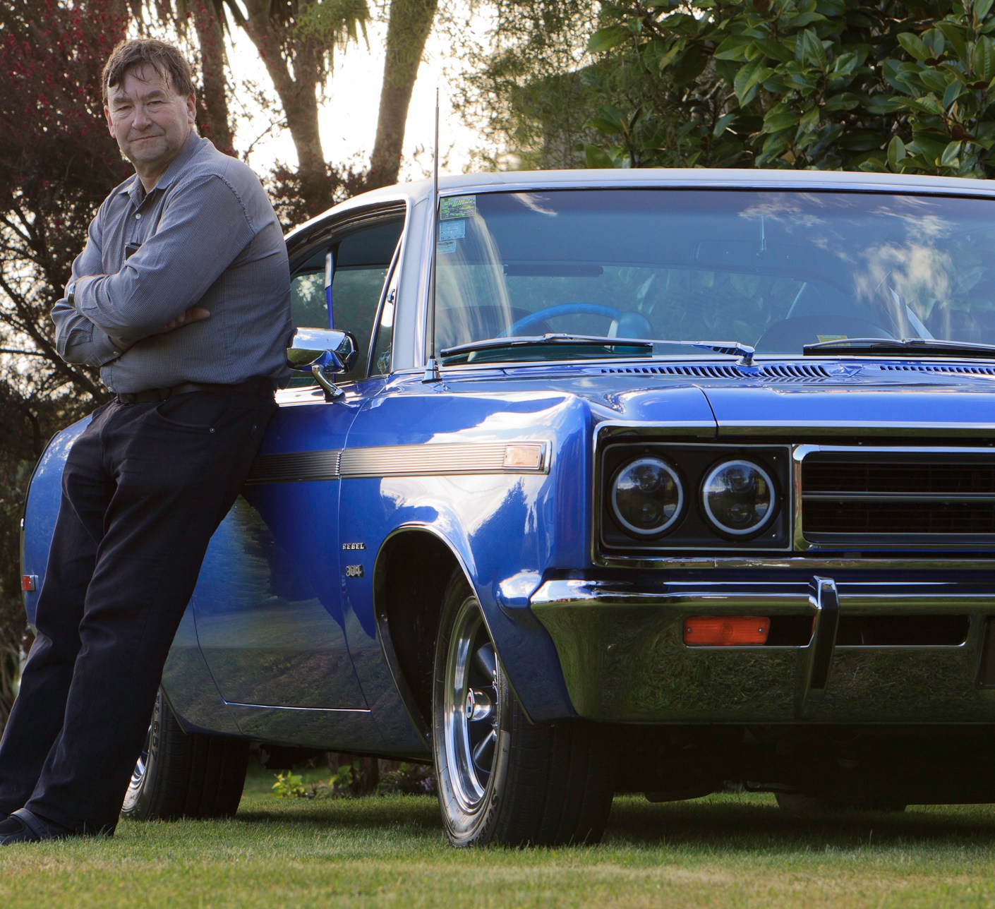 Lindsay McKenzie, with his restored 1970 Rambler Rebel SST in royal blue, leaning against the driver's door, showcasing the culmination of a 33-year quest.