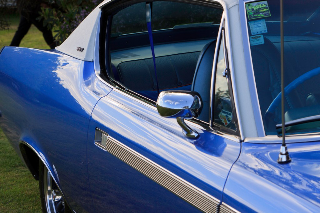 Interior view of a restored 1970 Rambler Rebel SST through the driver's door window, showing blue vinyl seats and the walnut dashboard.