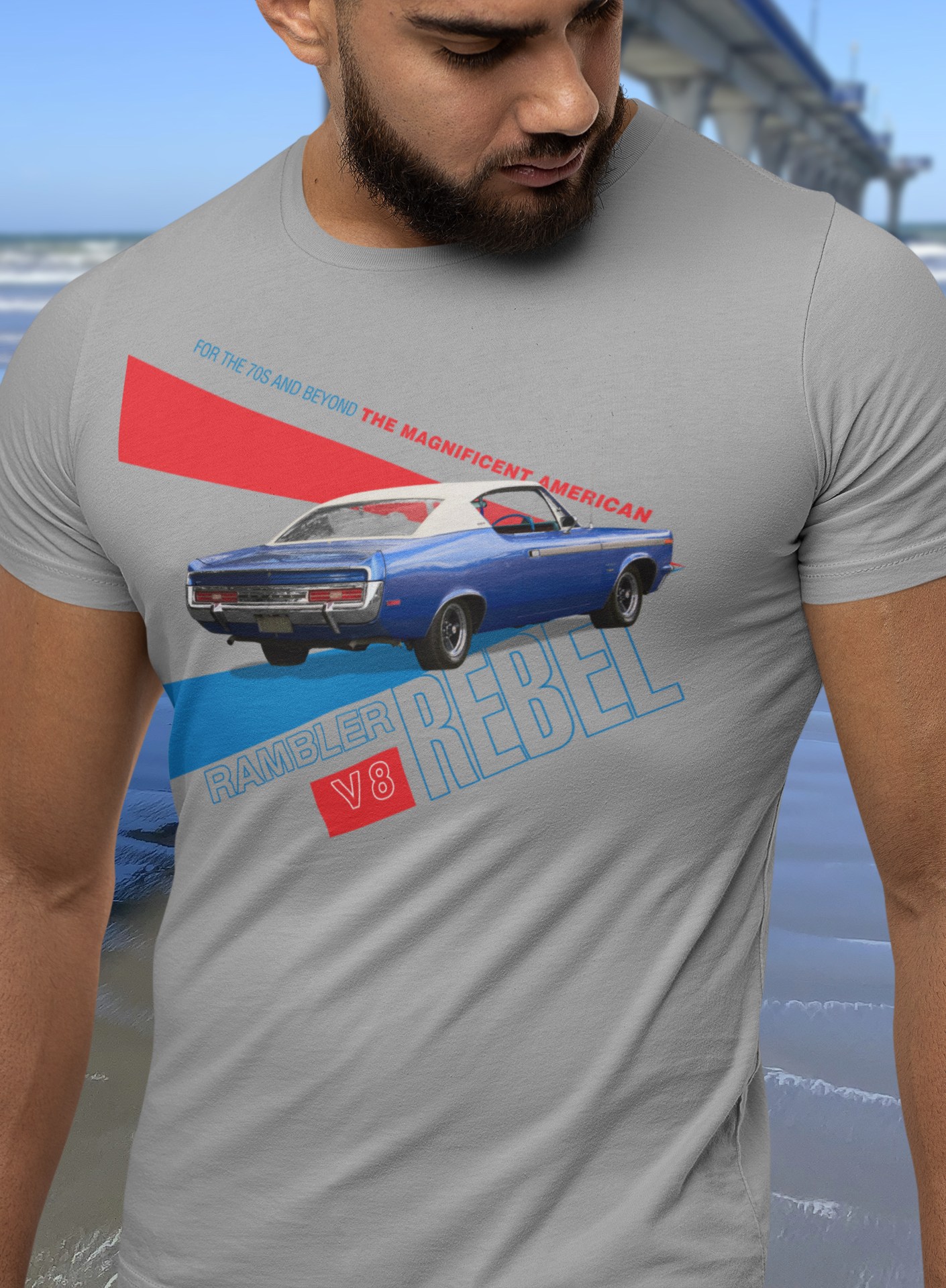 Bearded man in grey marle t-shirt with 1970 Rebel SST design stands beside New Brighton Pier, pointing symbolically towards Chile.