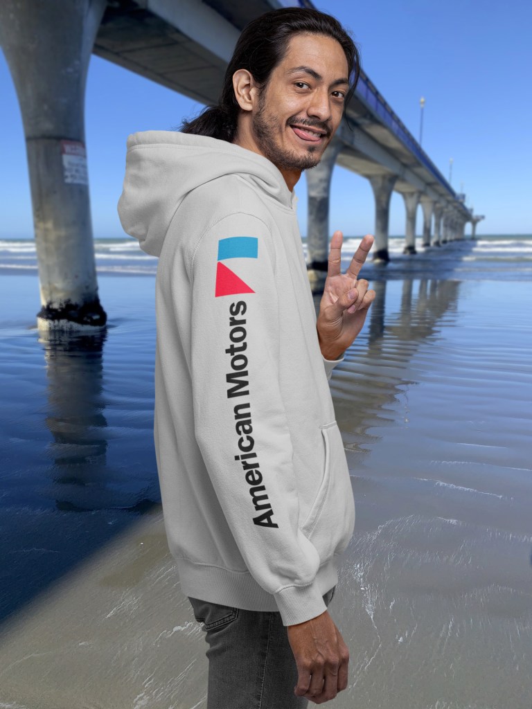 Man in grey marle hoodie with American Motors logo on sleeve and 1970 Rambler Rebel SST print on back, posing by New Brighton Pier.