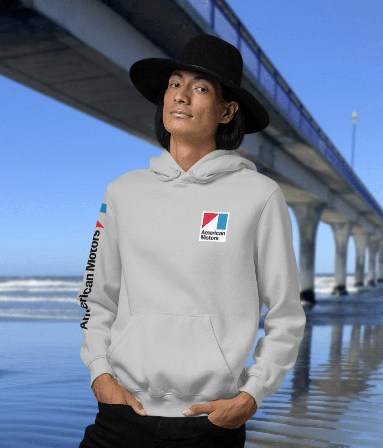 Man in grey marle hoodie with American Motors logo on the front, and the right sleeve who is standing near New Brighton Pier, showcasing the design on the opposite side.