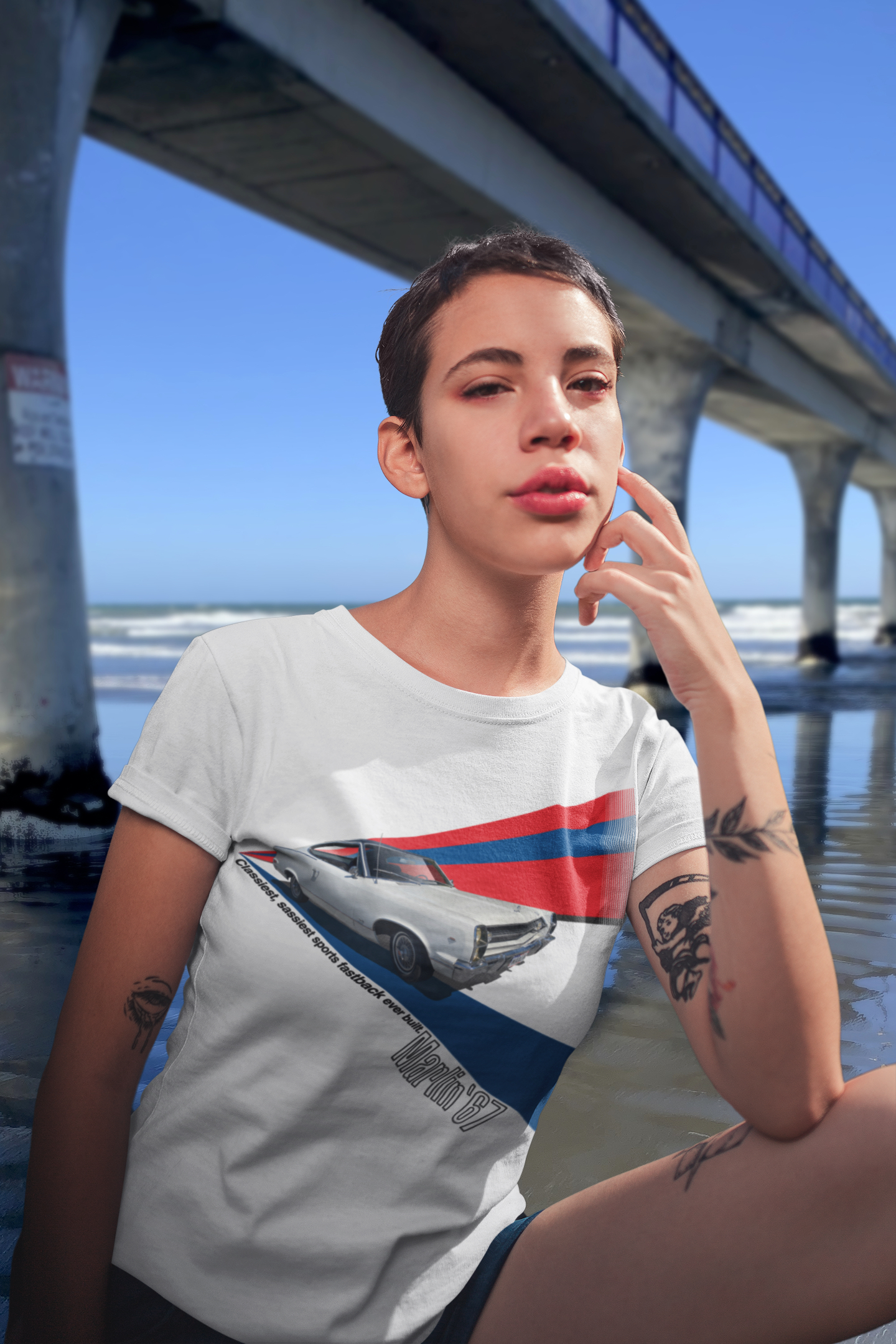 Woman wearing a white AMC Marlin t-shirt beside New Brighton Pier with clear blue sky.