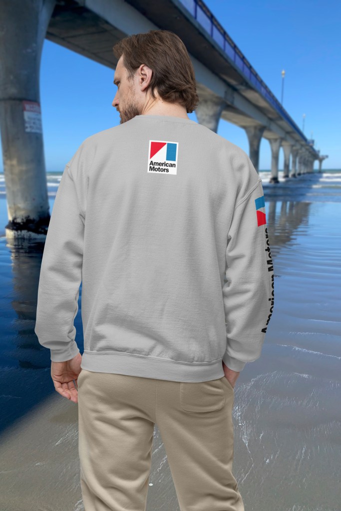 Man wearing grey marle long-sleeve t-shirt with 1970 Rambler Rebel SST design, featuring American Motors logos, beside New Brighton Pier.