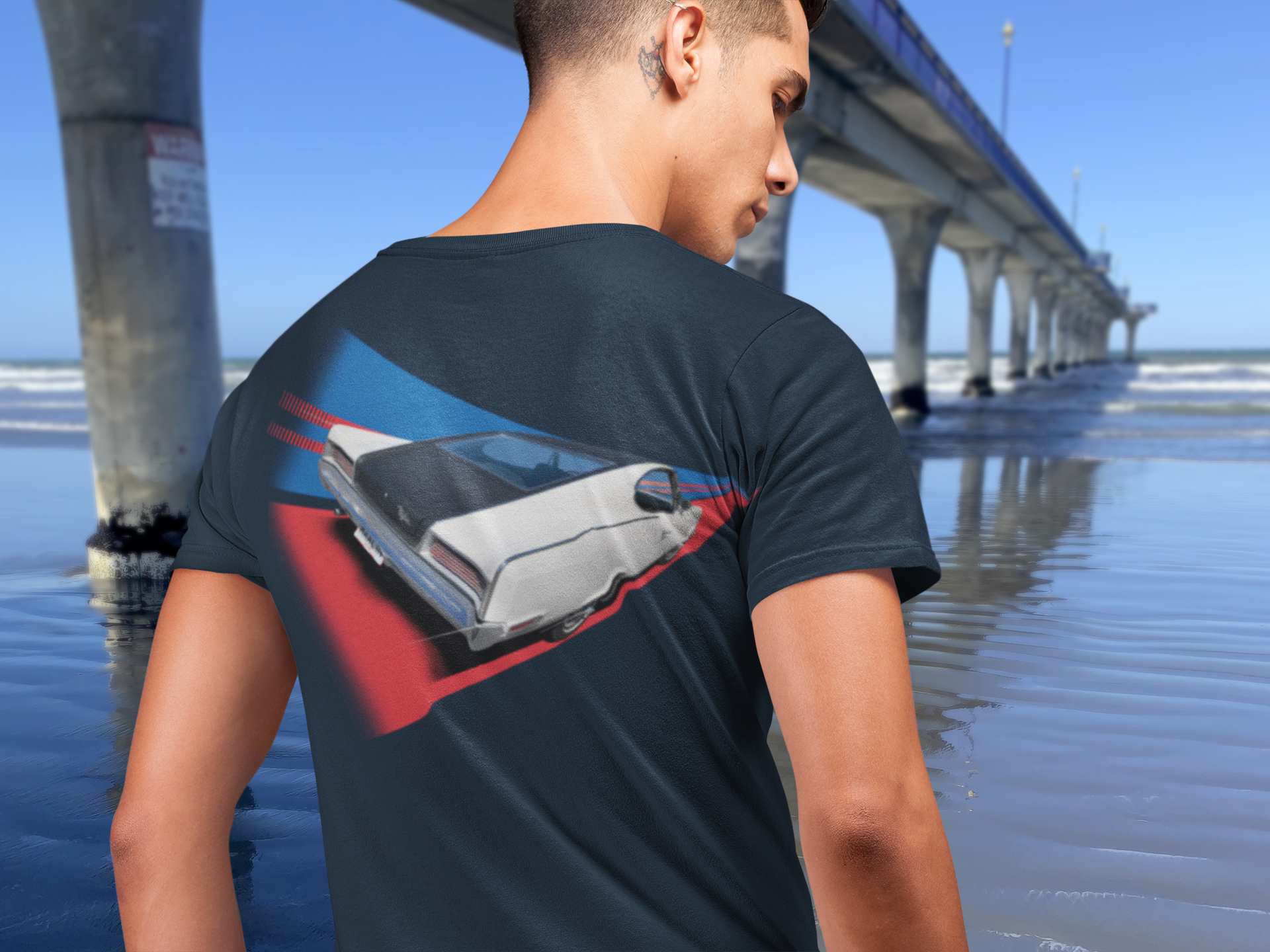 Man in navy blue t-shirt with 1967 AMC Marlin graphic standing next to New Brighton Pier.