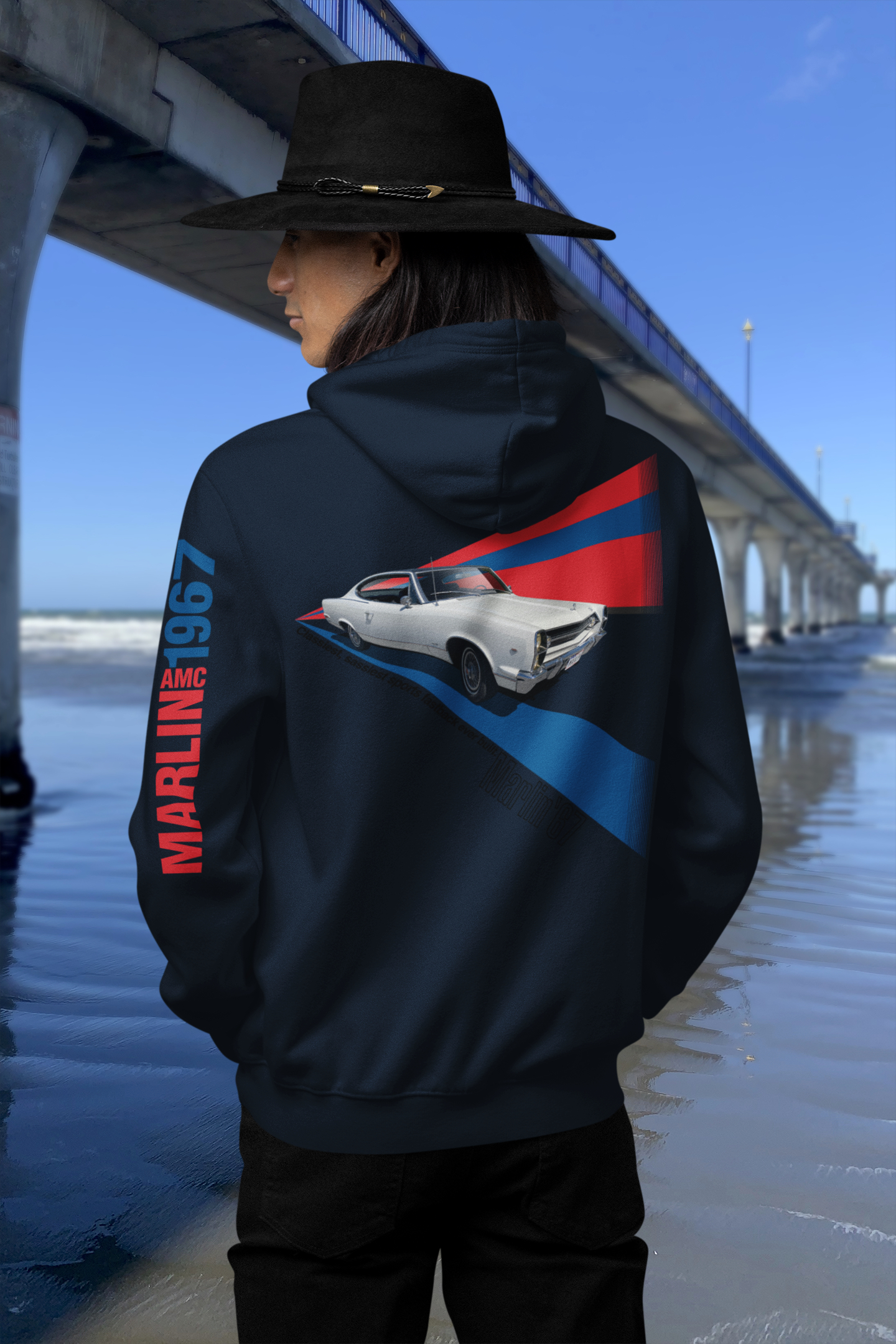 Back view of navy blue hoodie with 1967 AMC Marlin graphic beside New Brighton's concrete pier under a clear blue sky.