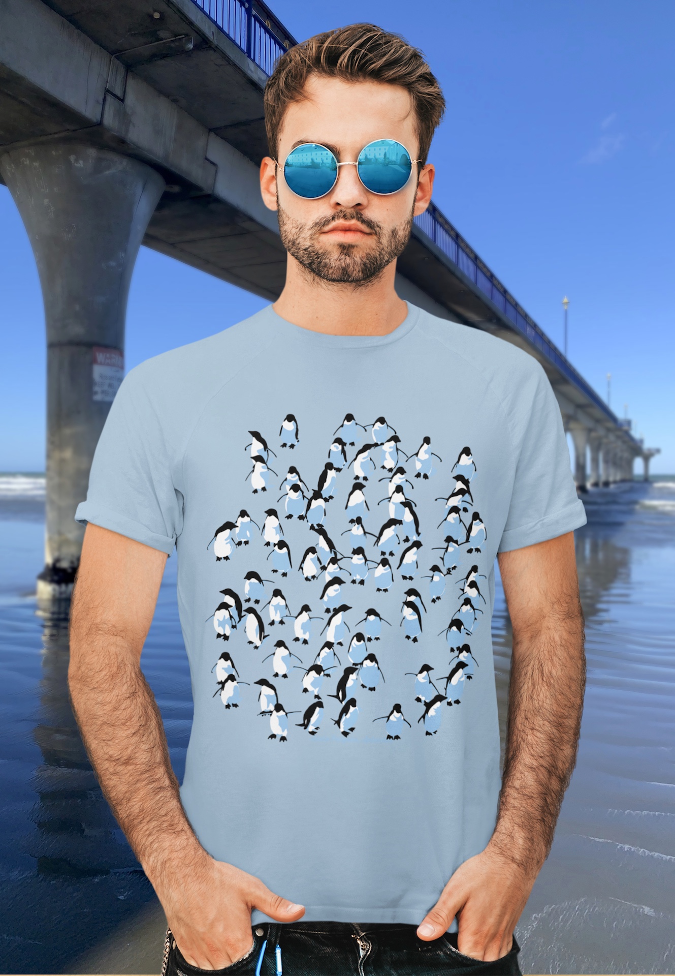 Bearded man with sunglasses in a pale blue Adelie Penguins t-shirt, posing beside the reinforced concrete New Brighton Pier.