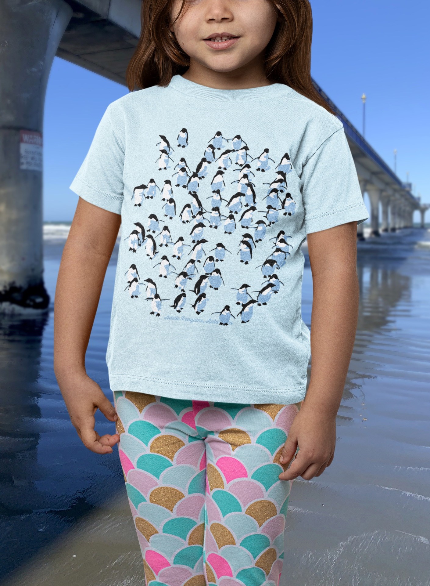 Little girl in a pale blue Adelie Penguin t-shirt beside New Brighton Pier.