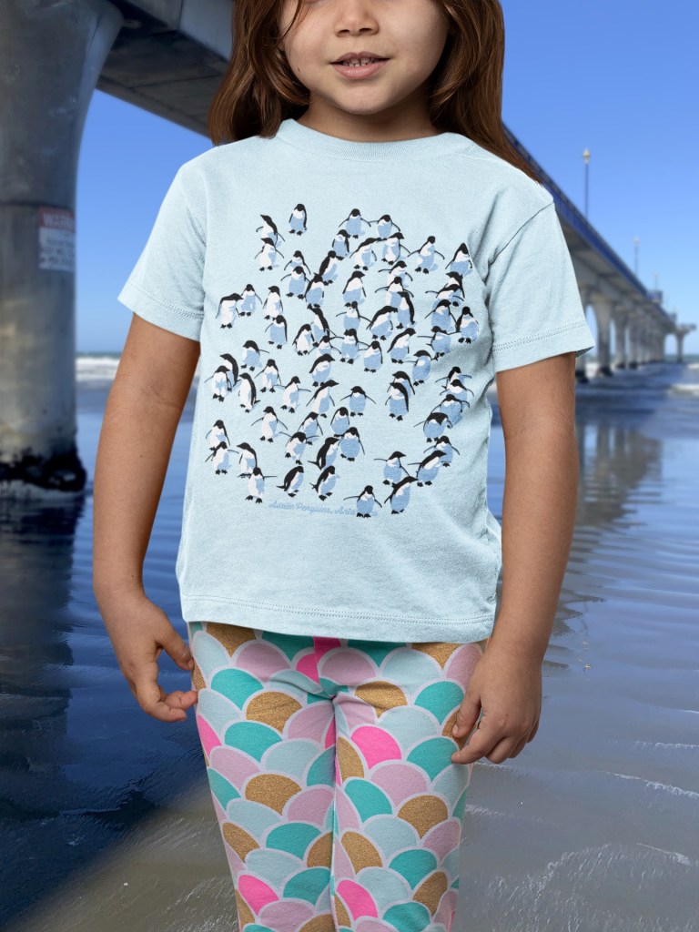 Little girl in a pale blue Adelie Penguin t-shirt beside New Brighton Pier.