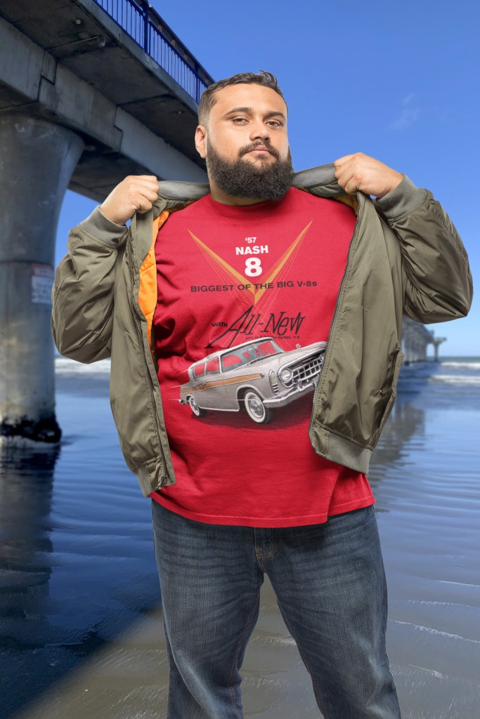 Man wearing a red 1957 Rambler t-shirt standing beside New Brighton Pier, celebrating the Rambler Rebel’s legacy.