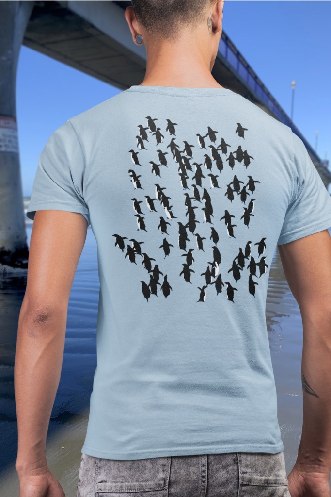 Back view of a man wearing a light blue Adelie Penguins t-shirt beside New Brighton Pier, showing penguins fleeing a leopard seal.